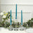 Teal taper candles in glass holders with greenery and flowers