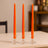 Three orange taper candles in clear glass holders on a table.