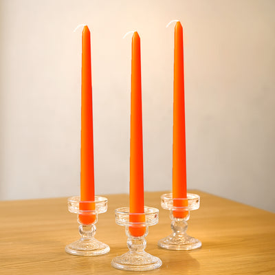 Three orange taper candles in glass holders on a wooden surface.
