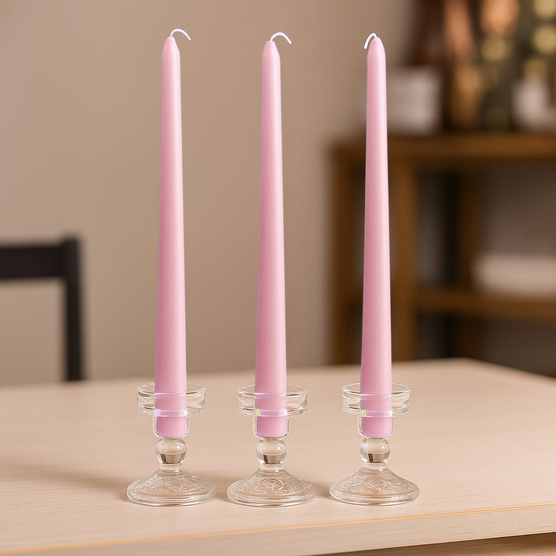 Three pink taper candles in clear glass holders on a wooden table.