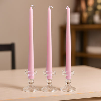 Three pink taper candles in clear glass holders on a wooden table.