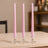 Three pink taper candles in clear glass holders on a wooden table.