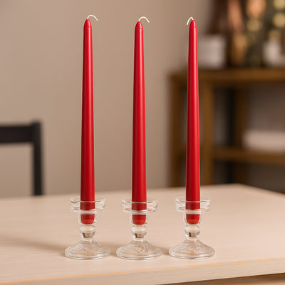 Three red taper candles in glass holders on a table.