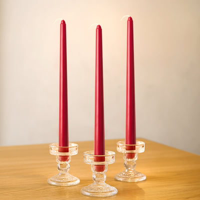 Three red tapered candles in clear glass holders on a wooden table.