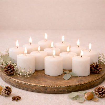 White pillar candles arranged on a rustic tray with greenery and pinecones.
