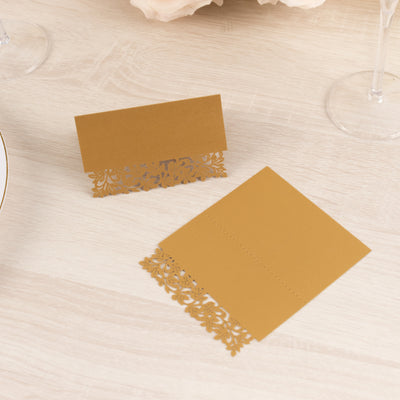 Elegant gold place cards with intricate lace design on a wooden table.