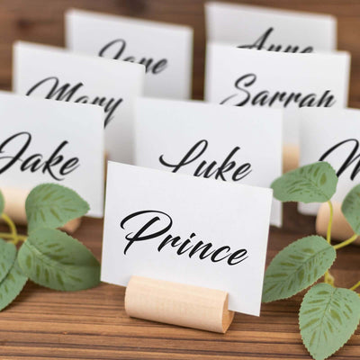 Personalized name place cards on wooden stands with greenery accents.