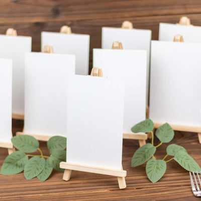 Mini easels with blank canvases and greenery on a wooden table.