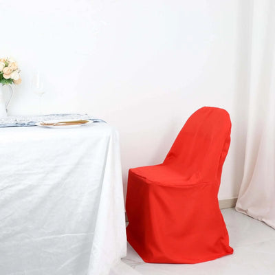Red chair cover draped on a chair beside a dining table.