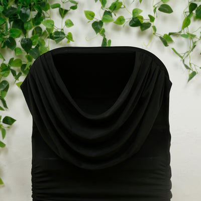 Black draped hooded dress on a mannequin with greenery backdrop.