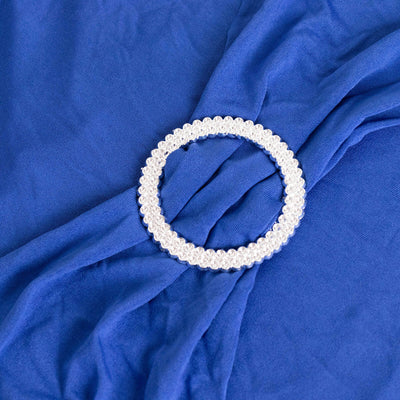 Decorative silver circular brooch resting on blue fabric.