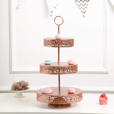 Three-tiered rose gold cake stand with decorative cutouts and macarons on top.