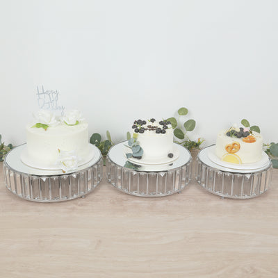 Three elegant birthday cakes with decorative toppings on mirrored stands.
