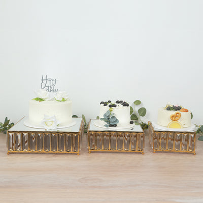 Elegant birthday cakes on decorative gold stands with greenery accents.
