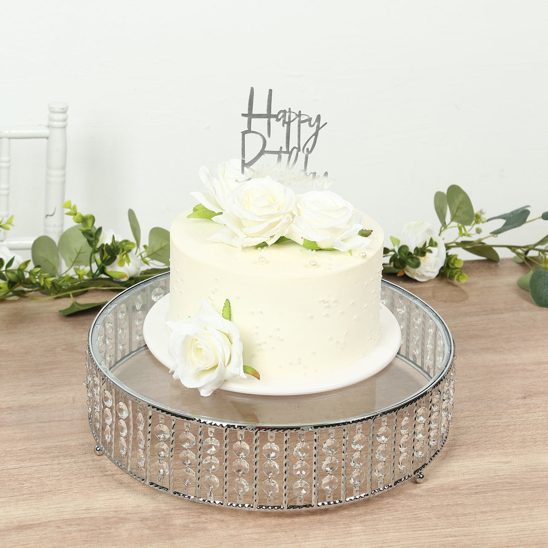 White floral cake with "Happy Birthday" topper on a decorative stand.
