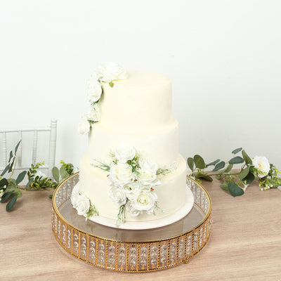 Three-tier white cake adorned with roses on a decorative mirror base.