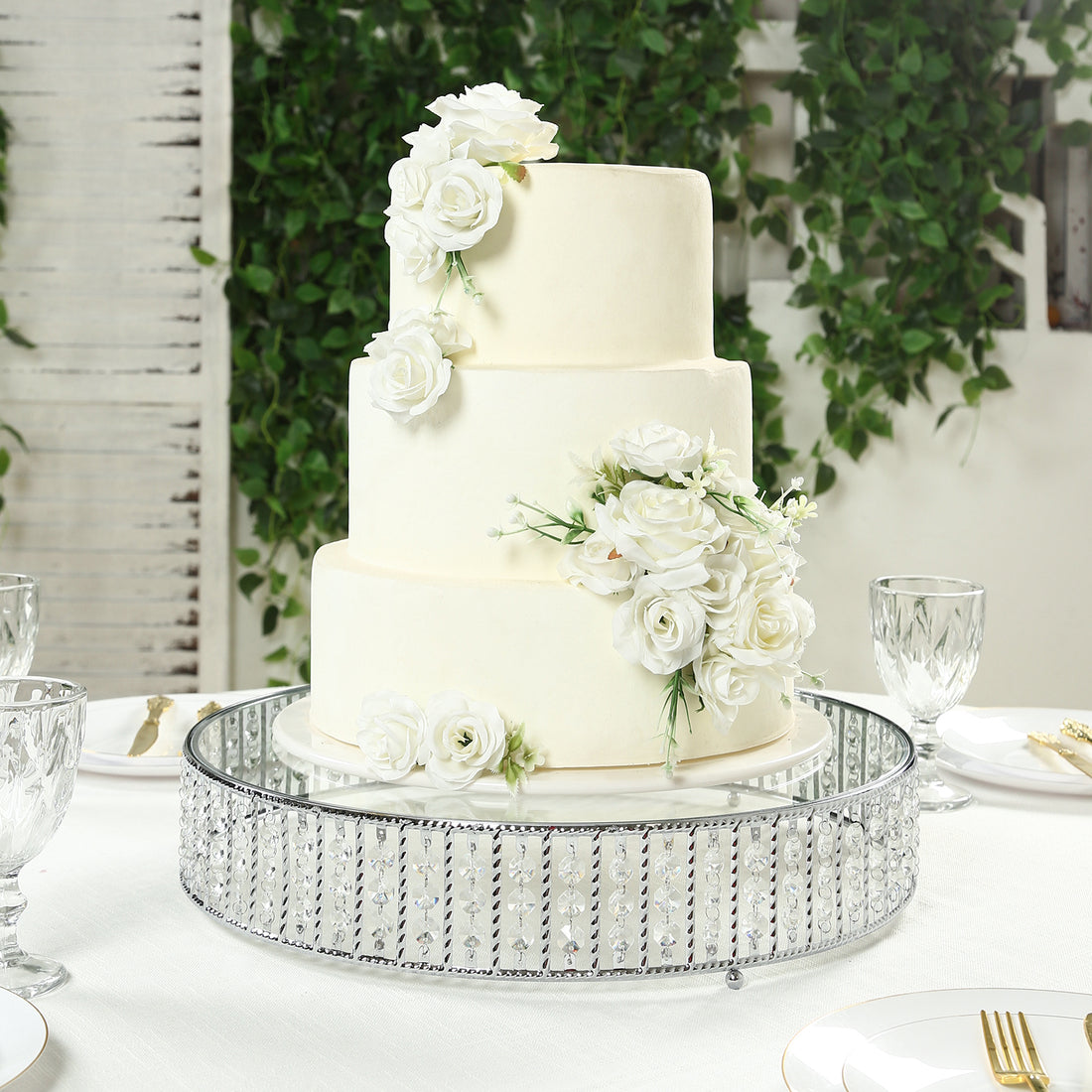 Elegant three-tier white wedding cake adorned with roses on a decorative stand.