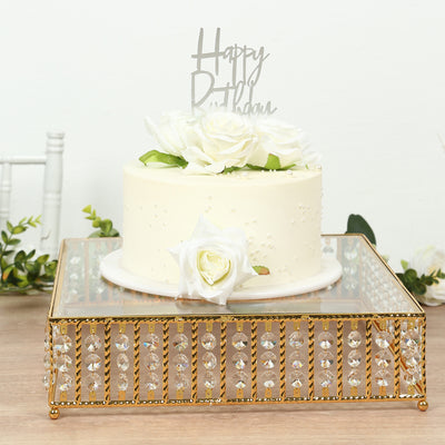 Birthday cake with white roses and "Happy Birthday" topper on a decorative stand.