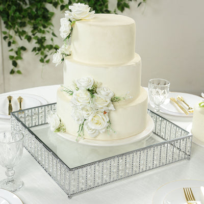 Elegant three-tier wedding cake adorned with white roses on a mirrored tray.