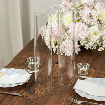 Clear glass vases on a wooden table with floral decor and tableware.