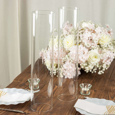 Clear glass vases on a wooden table with flowers in the background.
