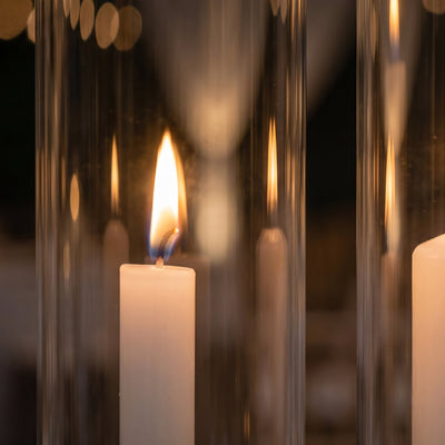 Lit white candle with warm flame reflected in glass on dark background