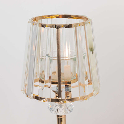 Elegant crystal lamp with gold accents and glass shade, illuminating a candle inside.