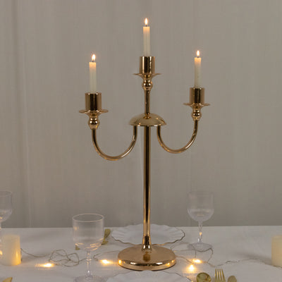 Gold three-arm candle holder with lit candles on a table setting.