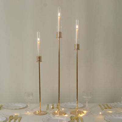 Elegant gold candle holders with glass tubes and candles on a dining table.