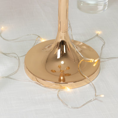 Rose gold lamp base with fairy lights on a textured surface.