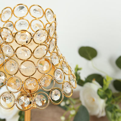 Gold crystal lamp shade with circular design and decorative flowers in the background.