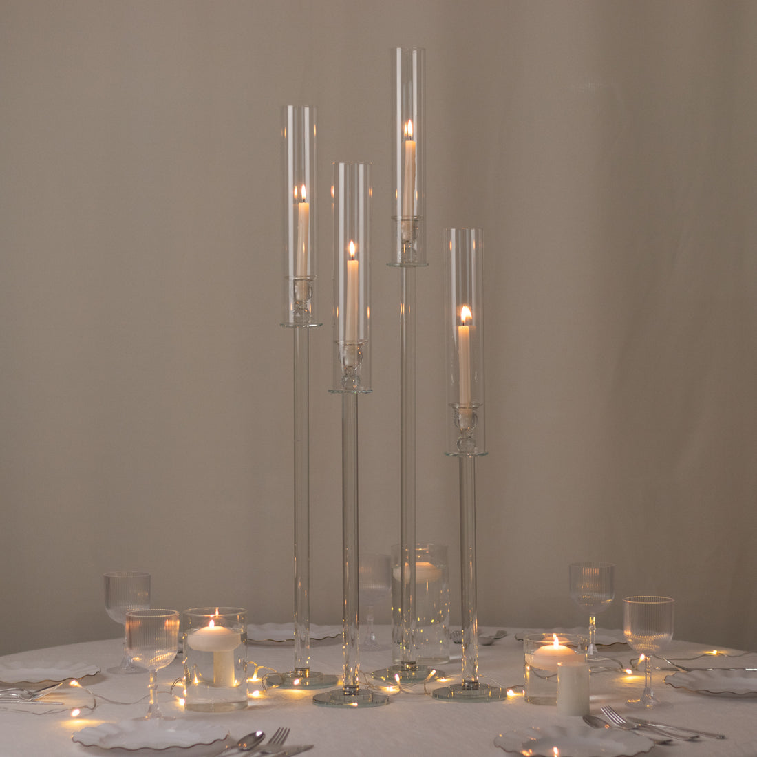 Elegant glass candle holders in varying heights with lit candles on a table setting.