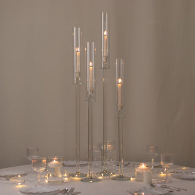 Elegant glass candle holders in varying heights with lit candles on a table setting.
