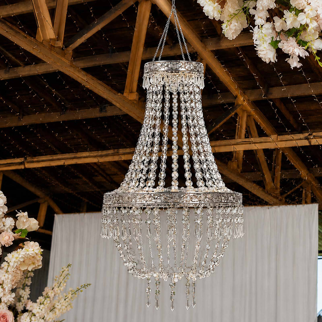 Elegant silver crystal chandelier hanging from rustic wooden ceiling at wedding venue