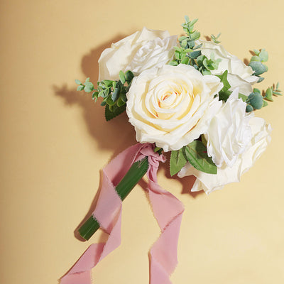 White rose bouquet with greenery and a pink ribbon on a yellow background.