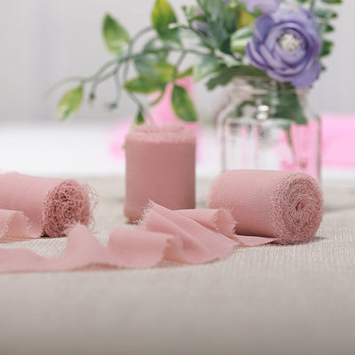 Pink fabric rolls and scraps arranged with a flower vase in a soft setting.