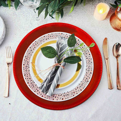 Elegant table setting with red charger plate, white and gold plates, and decorated napkin.