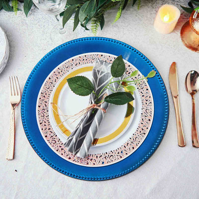 Elegant table setting with blue and gold plates, napkin, and greenery centerpiece.