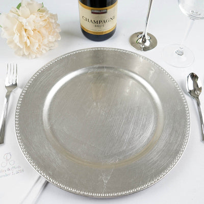 Elegant silver charger plate on a dining table setting with champagne and flowers.