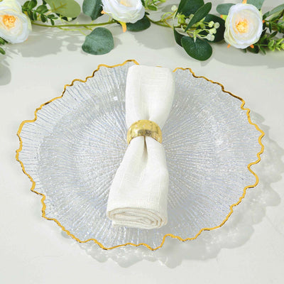 Elegant clear glass plate with gold rim and white napkin holder on a neutral background.