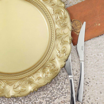 Elegant gold decorative plate with silver cutlery on a sequin backdrop.