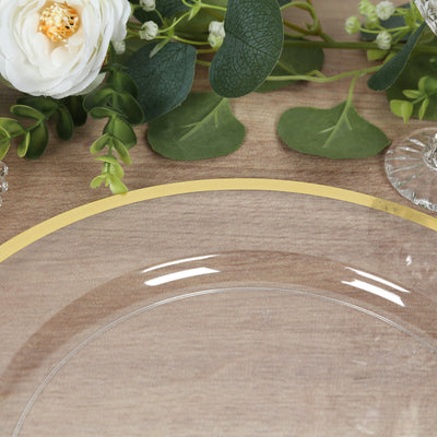 Elegant clear plate with a gold rim, surrounded by greenery and floral decor.
