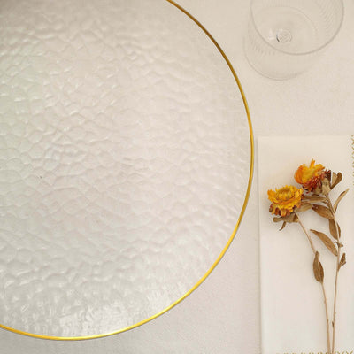 Clear glass plate with gold rim beside dried flowers and a glass.
