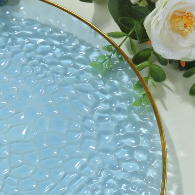 Textured blue plate with gold rim, surrounded by greenery and flowers.
