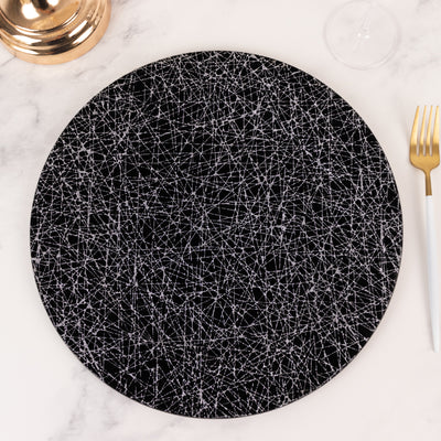 Black round placemat with white geometric pattern on marble table.