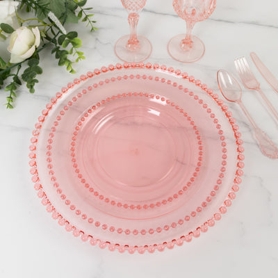 Pink glass dinnerware set with beaded edges on a marble table.