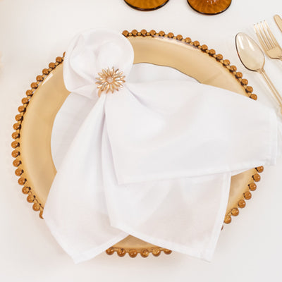 Elegant white napkin with decorative ring on a gold plate.