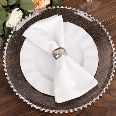Elegant table setting with white napkin and silver holder on decorative plate.
