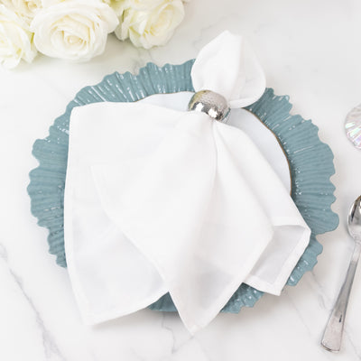 Elegant white napkin on a decorative teal plate with a silver napkin ring.