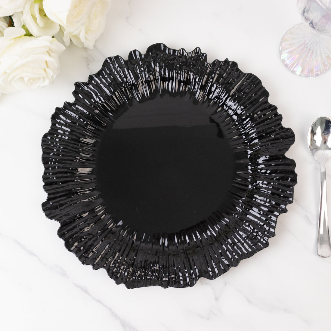 Black decorative plate with ruffled edges on a marble surface.